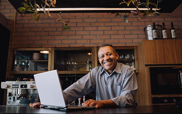 a mature male cafe owner smiling behind the counter with laptop